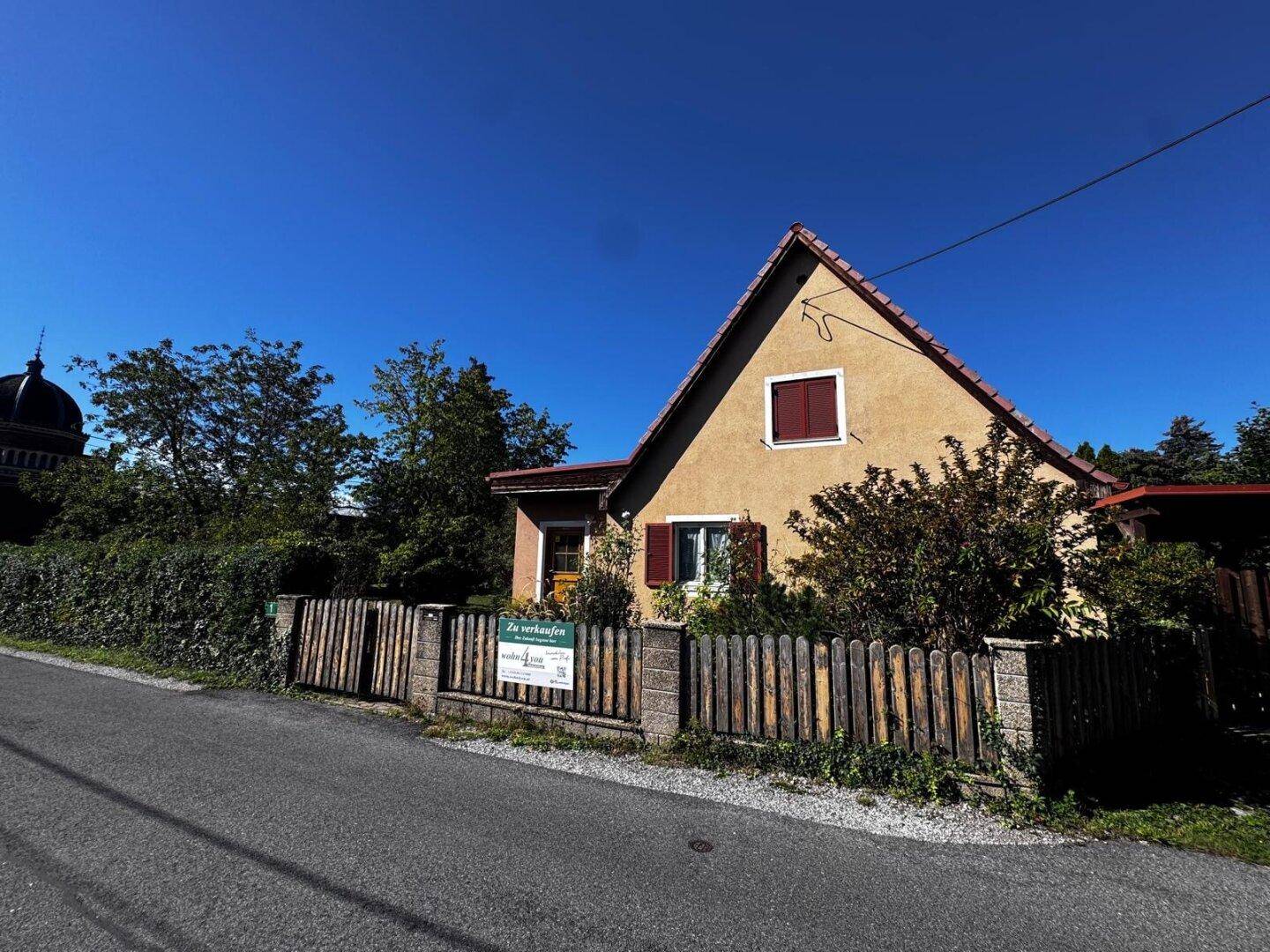 Charmantes Einfamilienhaus mit Satteldach und braunen Fensterläden, umgeben von einem Holzzaun.