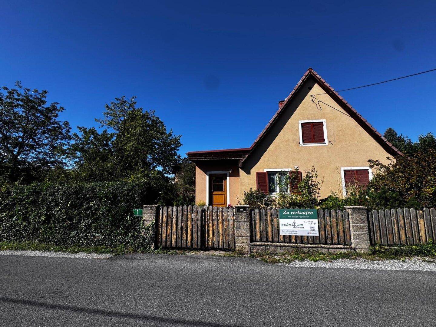 Vorderansicht des Hauses mit Holzzaun und gepflegtem Vorgarten unter blauem Himmel.