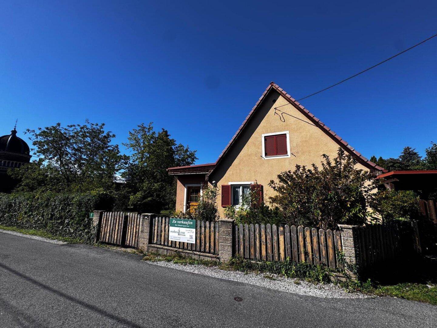 Einfamilienhaus mit traditionellem Satteldach und braunen Fensterläden, von der Straße aus sichtbar.