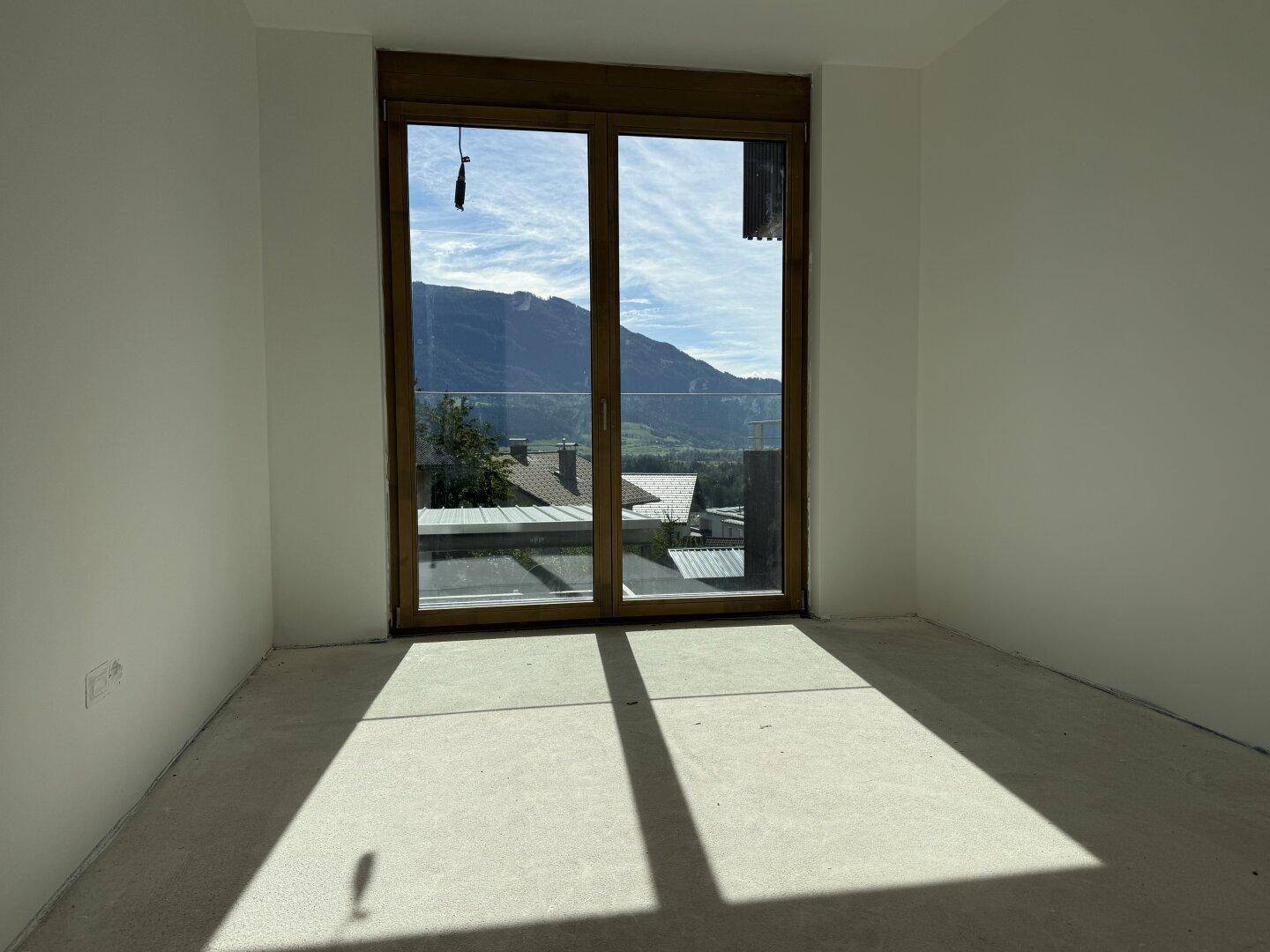 Unfertiger Raum mit viel Tageslicht und Zugang zu einem Balkon mit Bergblick.