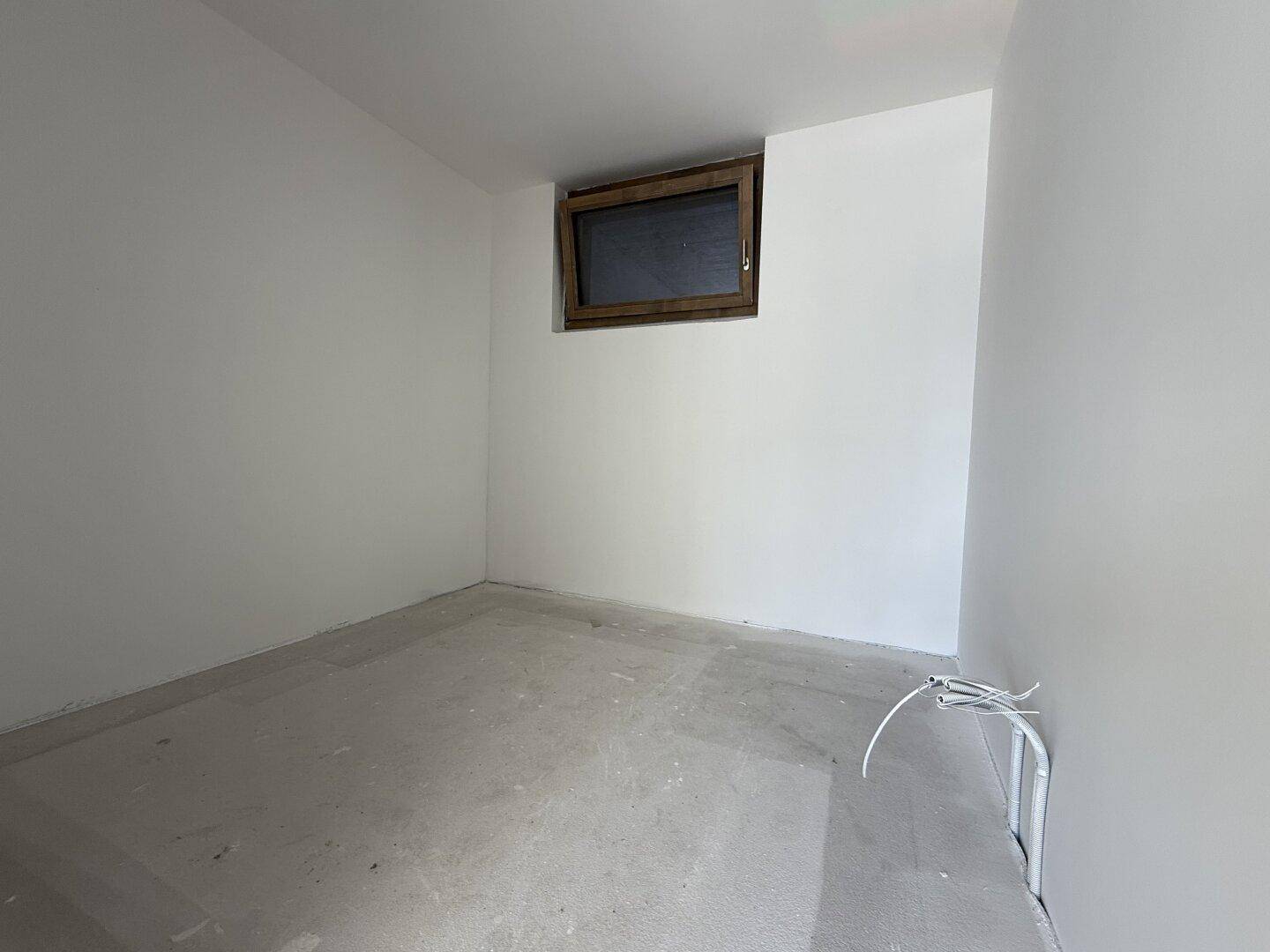 Leerer, unfertiger Raum mit einem kleinen Fenster, bereit für den Ausbau.