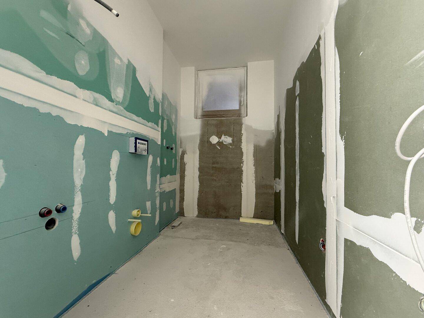 Unfertiges Badezimmer mit Trockenbauwänden und vorbereiteten Sanitäranschlüssen.