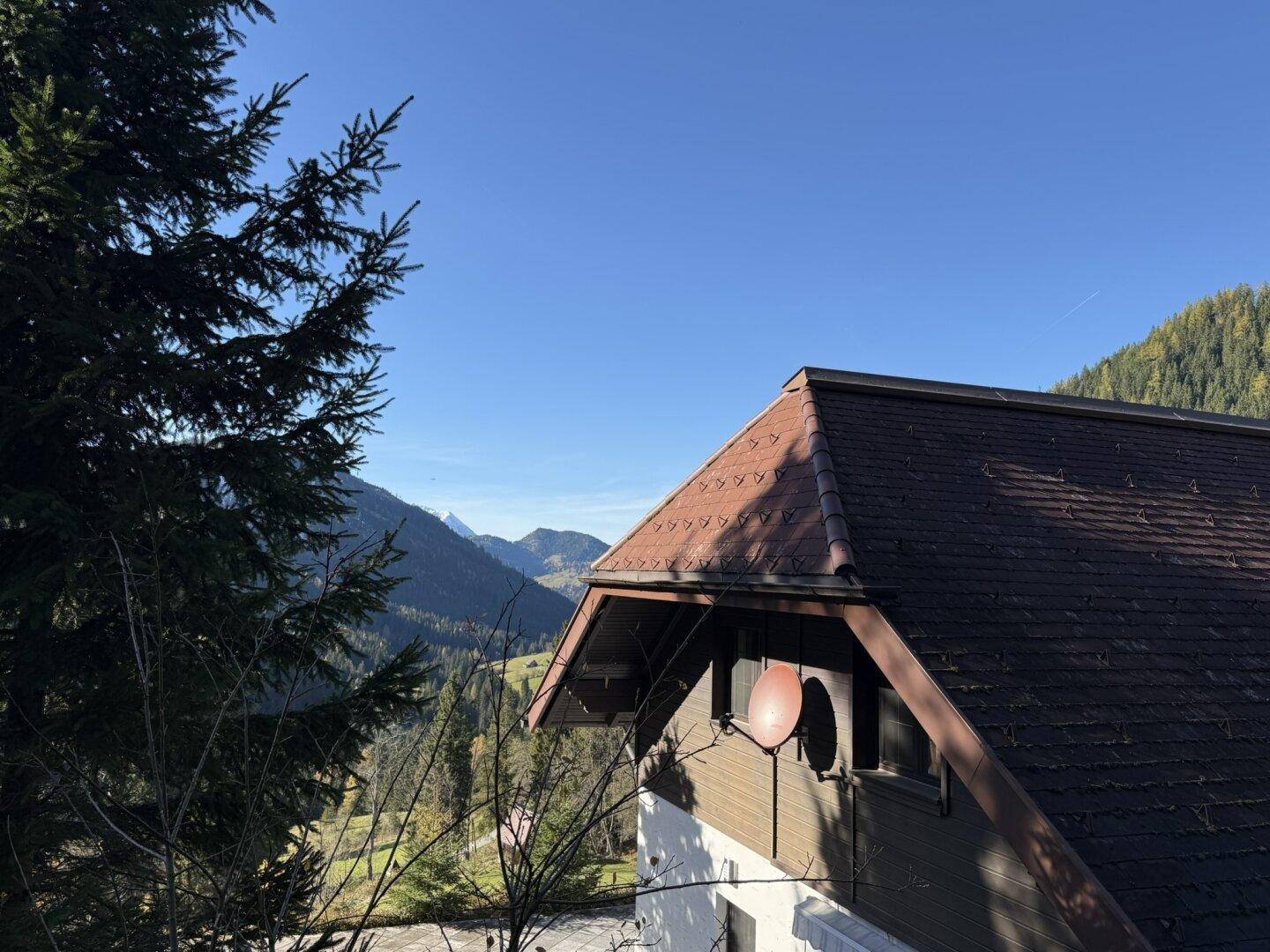 Traditionelles Hausdach mit Ziegeln und Satellitenschüssel vor einer malerischen Bergkulisse.