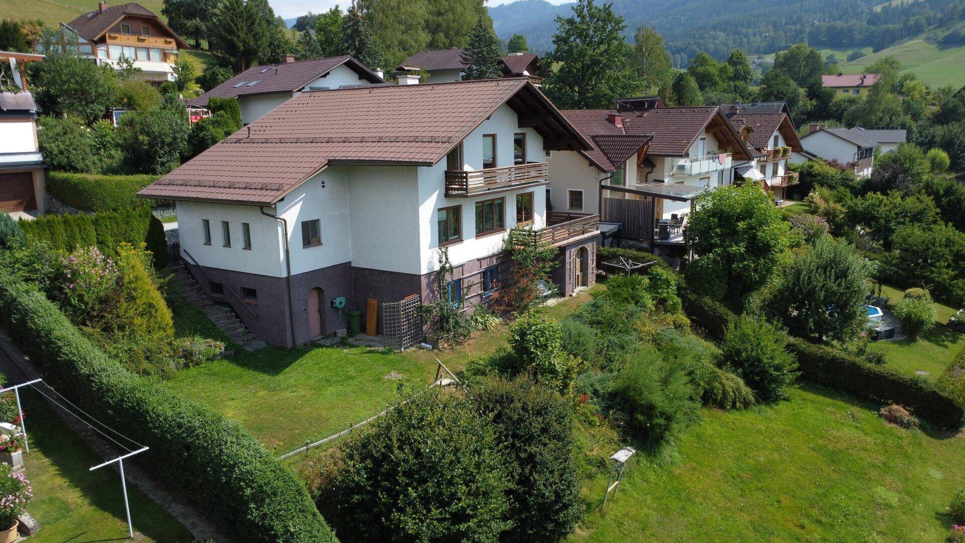 Wohnhaus in idyllischer Hanglage mit Terrassen und Garten, umgeben von grüner Natur und weiteren Häusern.