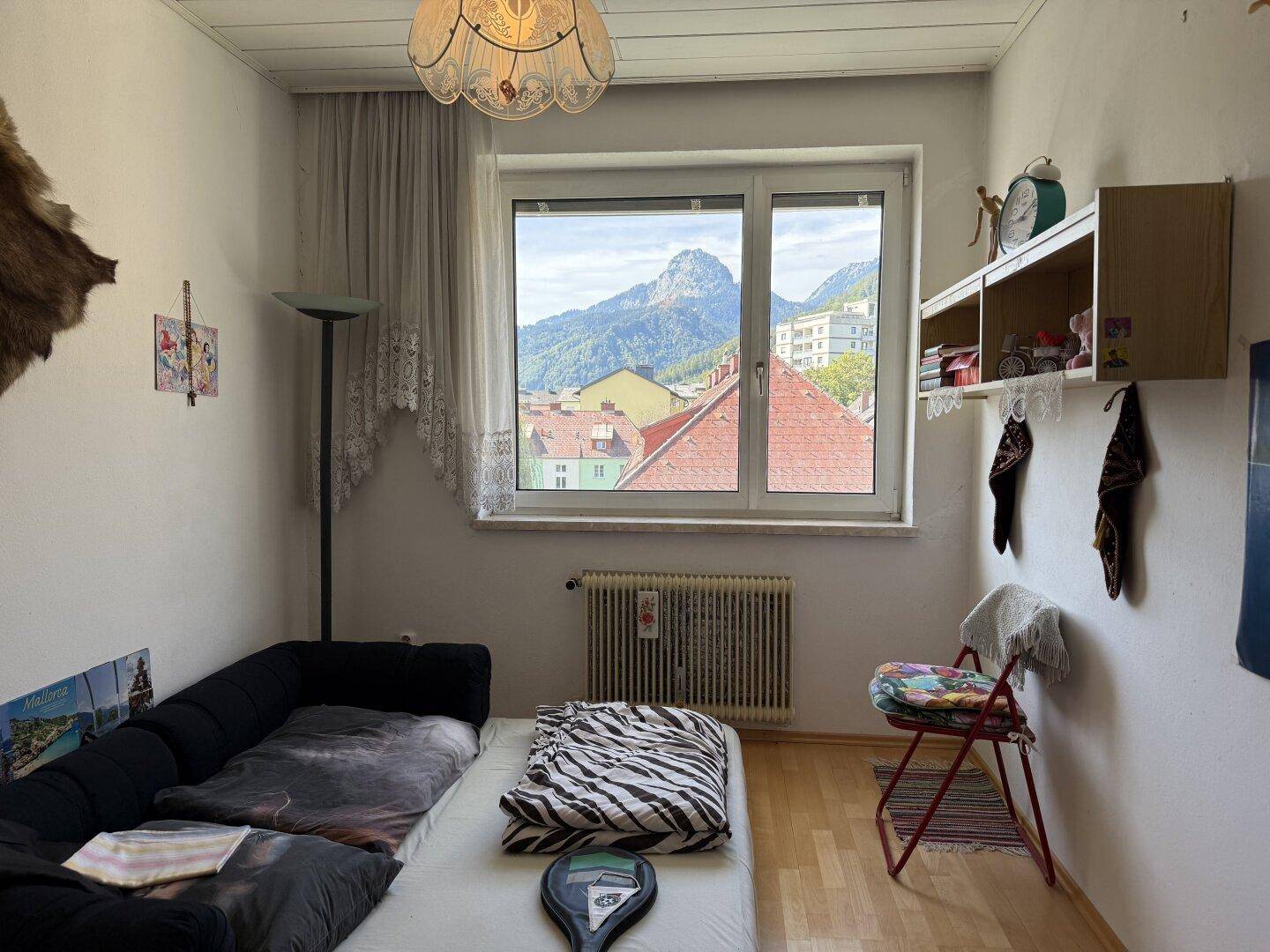Helles Schlafzimmer mit Einzelbett, Holzboden und einem schönen Ausblick auf die umliegende Berglandschaft.
