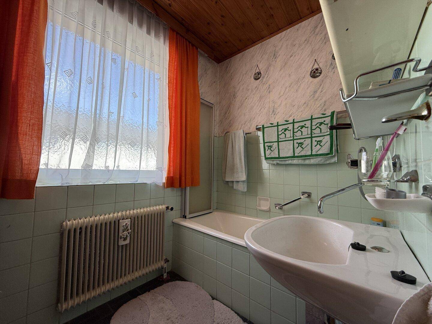 Badezimmer mit hellgrünen Fliesen, Badewanne mit Duschvorhang, Waschbecken und Fenster für Tageslicht.