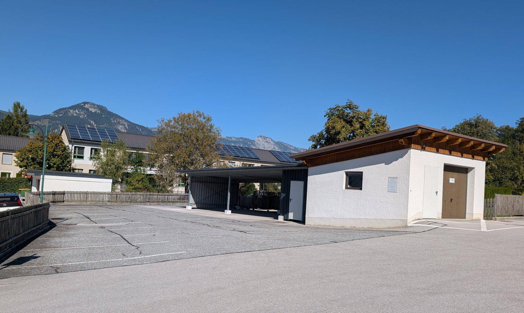Carport und Nebengebäude mit Blick auf weitere Gebäude mit Solaranlagen und Berge.