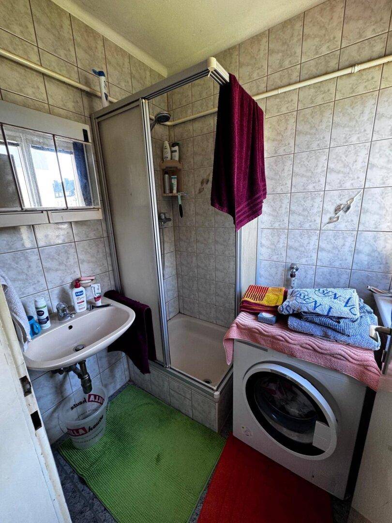Kleines gefliestes Badezimmer mit Duschkabine, Waschbecken, Spiegelschrank und Waschmaschine.