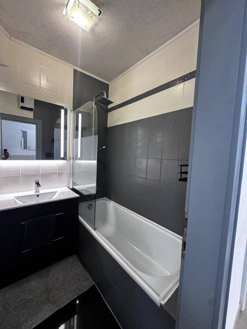Modernes Badezimmer mit Badewanne, Duschabtrennung und dunklen Fliesen an den Wänden.