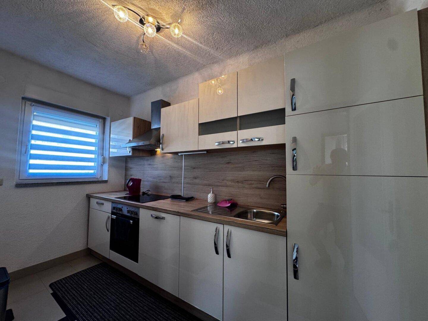 Moderne Küche mit glänzenden beigen Schränken, Holzarbeitsplatte und integrierten Geräten.