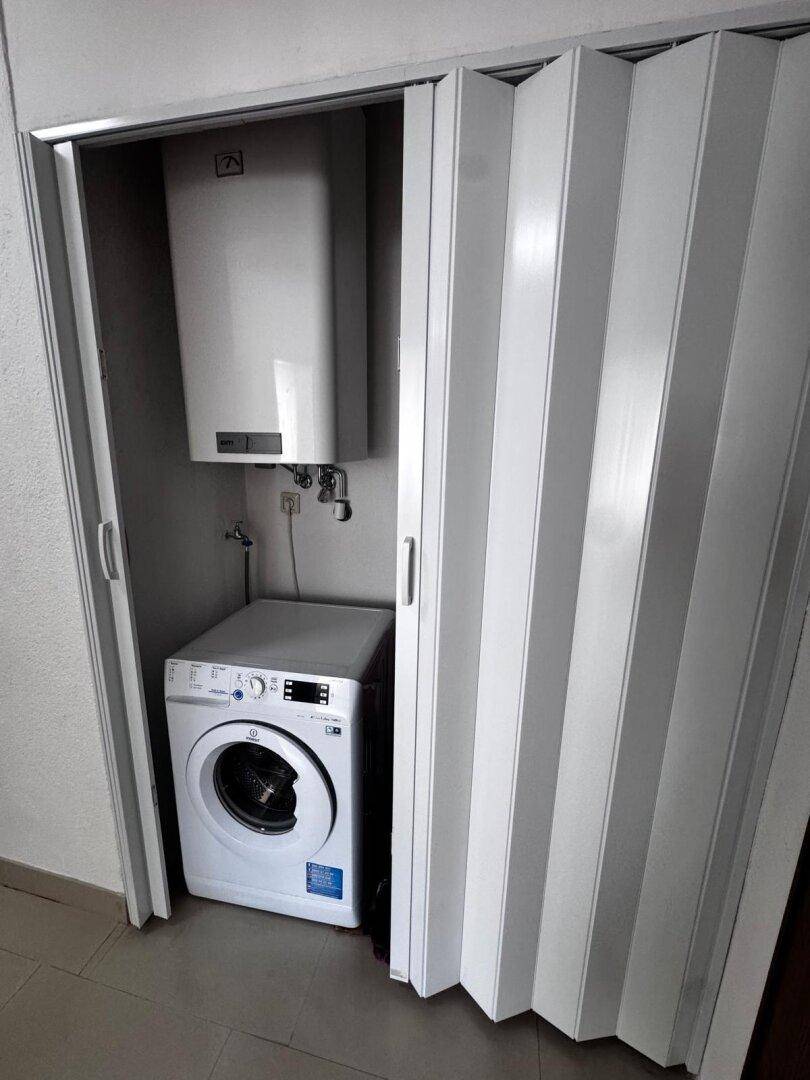 Praktischer Abstellraum mit Waschmaschine und Warmwasserboiler hinter Falttüren.