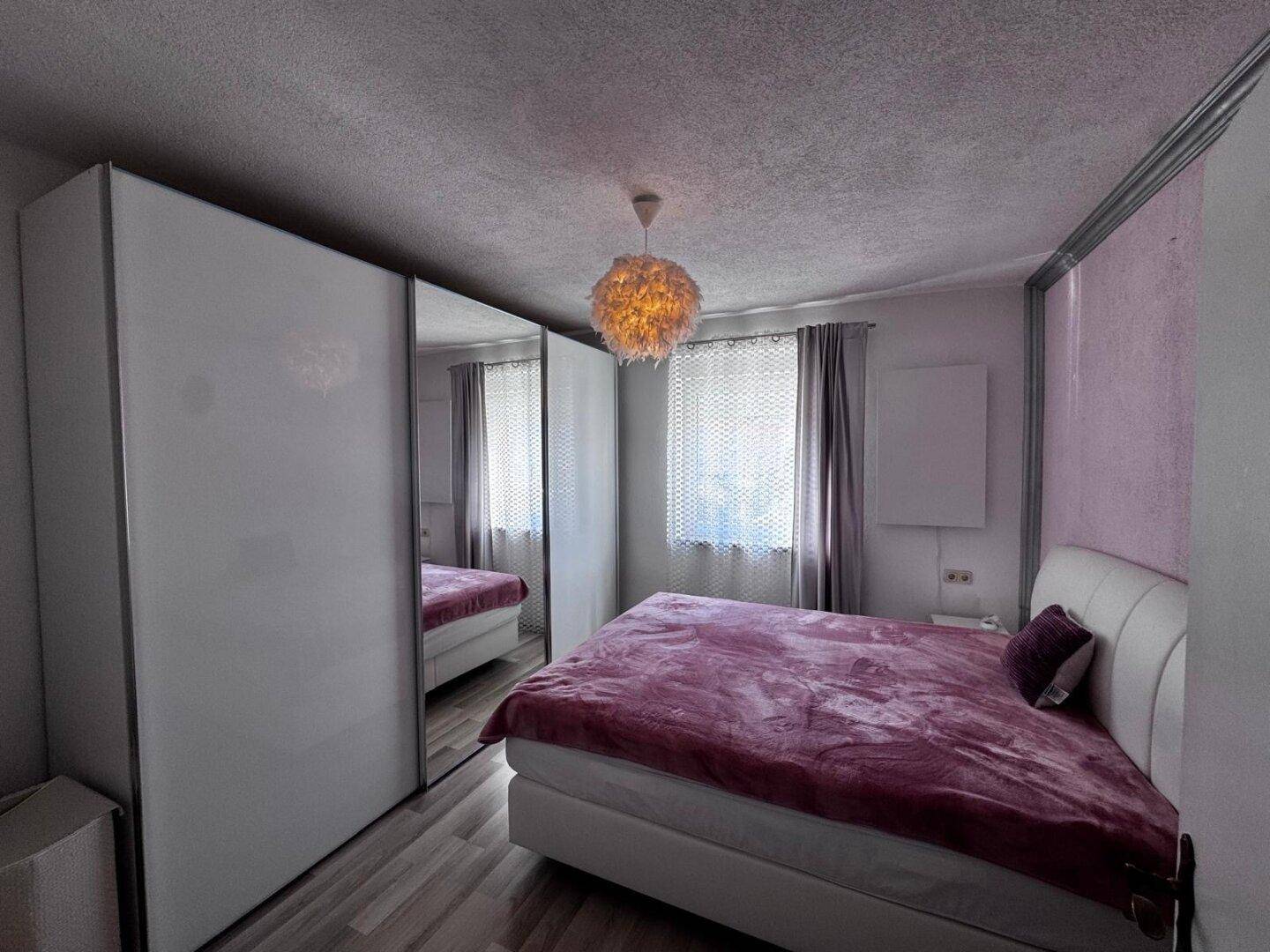Gemütliches Schlafzimmer mit großem Bett, Spiegelschränken und lila Bettwäsche.