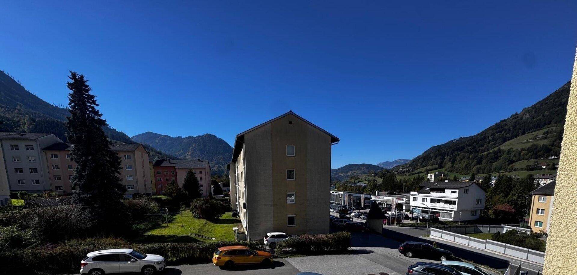 Panoramablick auf die umliegende Berglandschaft mit Wohngebäuden und blauem Himmel.