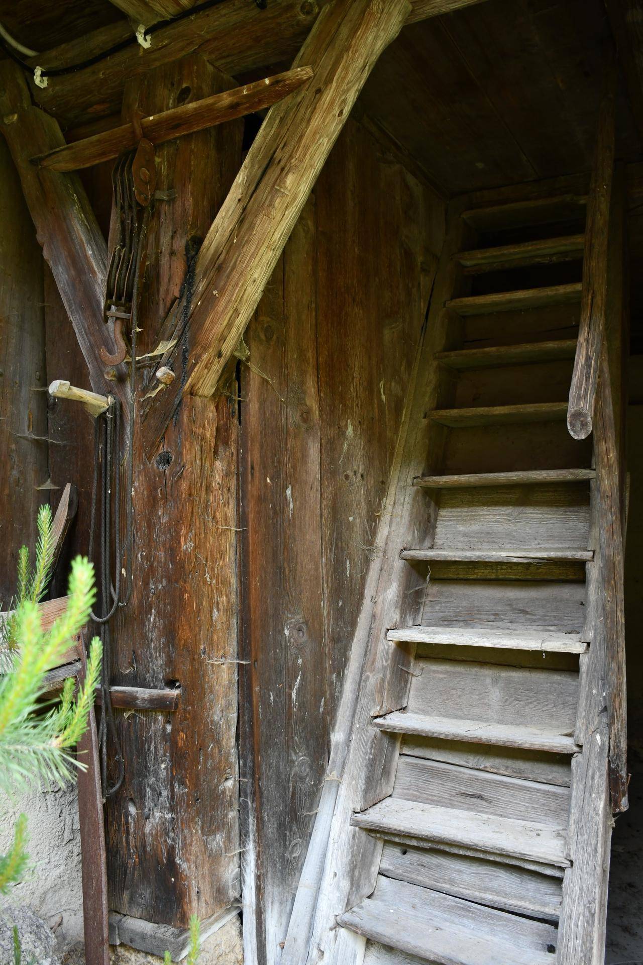 Alte, rustikale Holztreppe in einem scheunenartigen Raum mit groben Holzwänden und Balken.