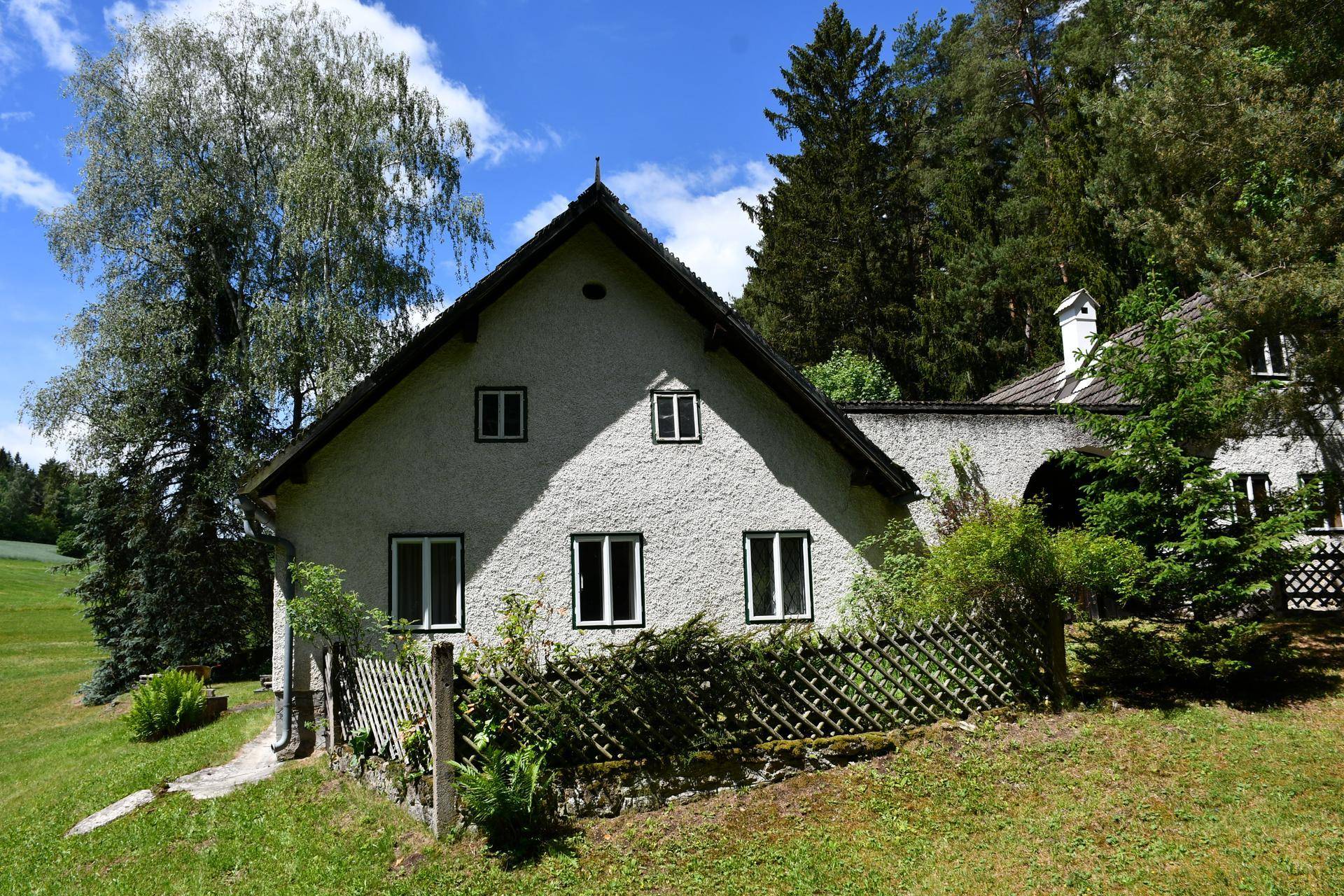 Traditionelles Landhaus mit weißer Fassade und grüner Hecke im Vordergrund.