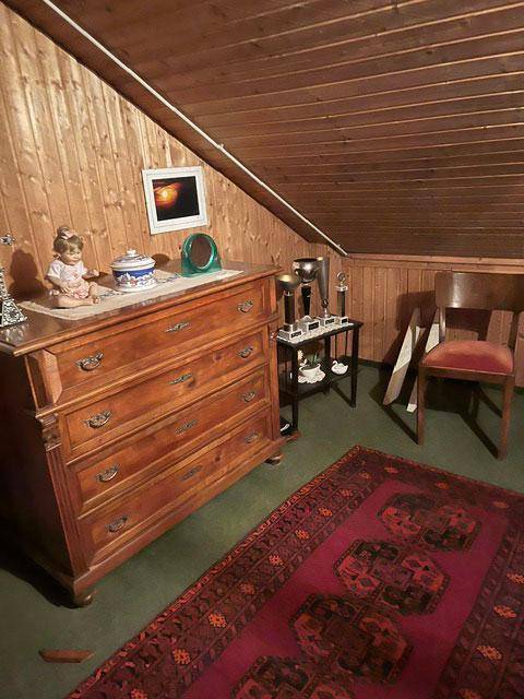 Dachgeschosszimmer mit schrägen Wänden, Holztäfelung und antiker Kommode.