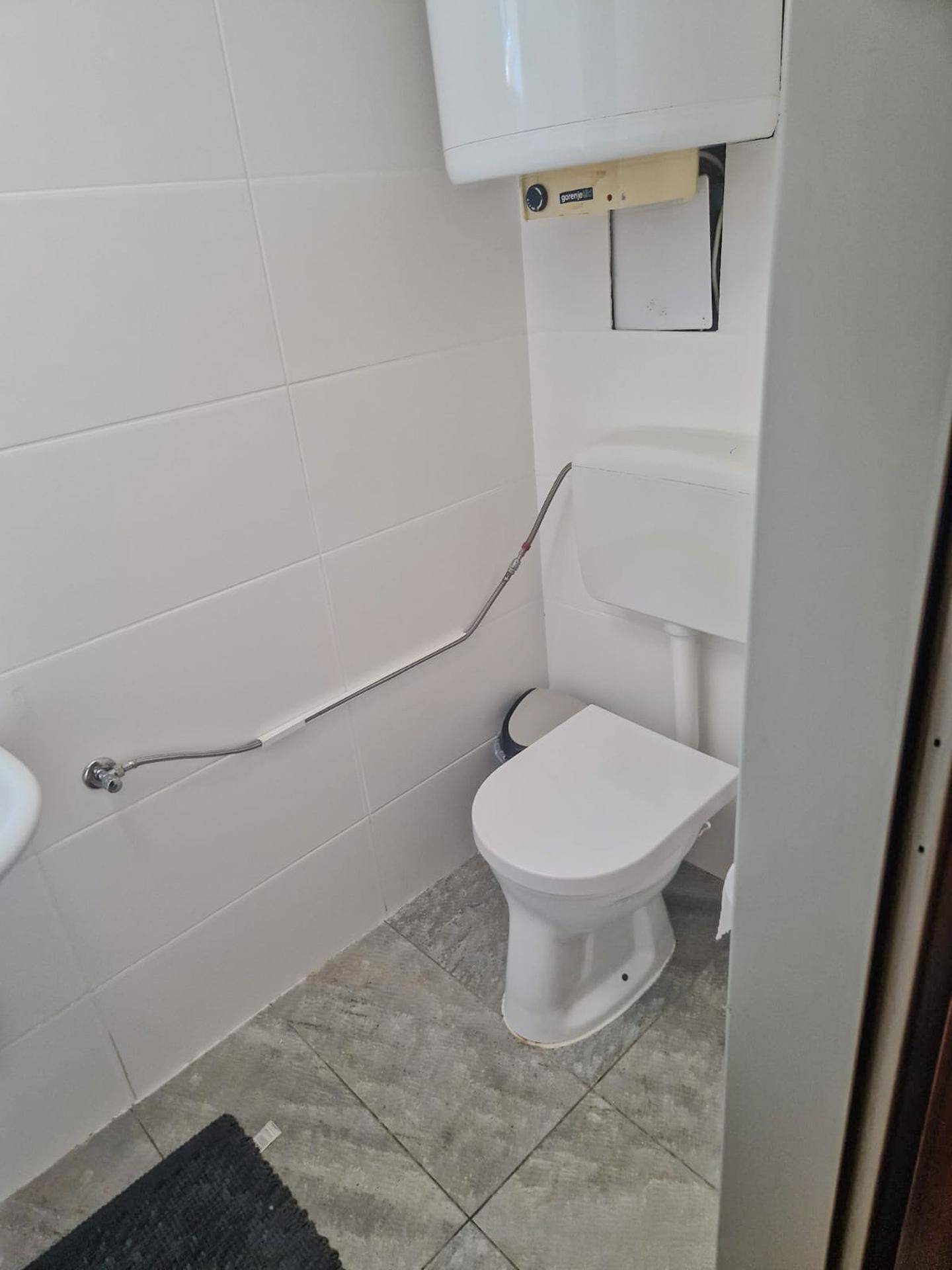 Kleines WC mit Toilette, Waschbecken und Haltegriff, komplett gefliest in Weiß.
