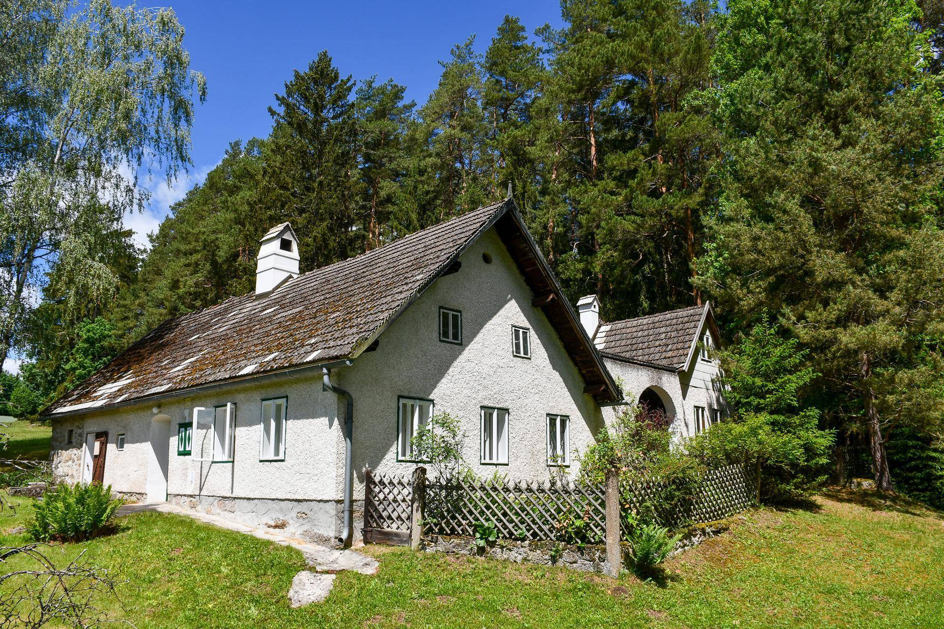Traditionelles Landhaus mit weißer Fassade und Satteldach, umgeben von grüner Natur und Wald.