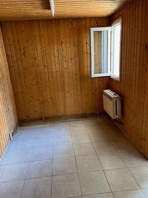 Kleiner Raum mit Holztäfelung, Fliesenboden und einem Heizkörper unter dem Fenster.