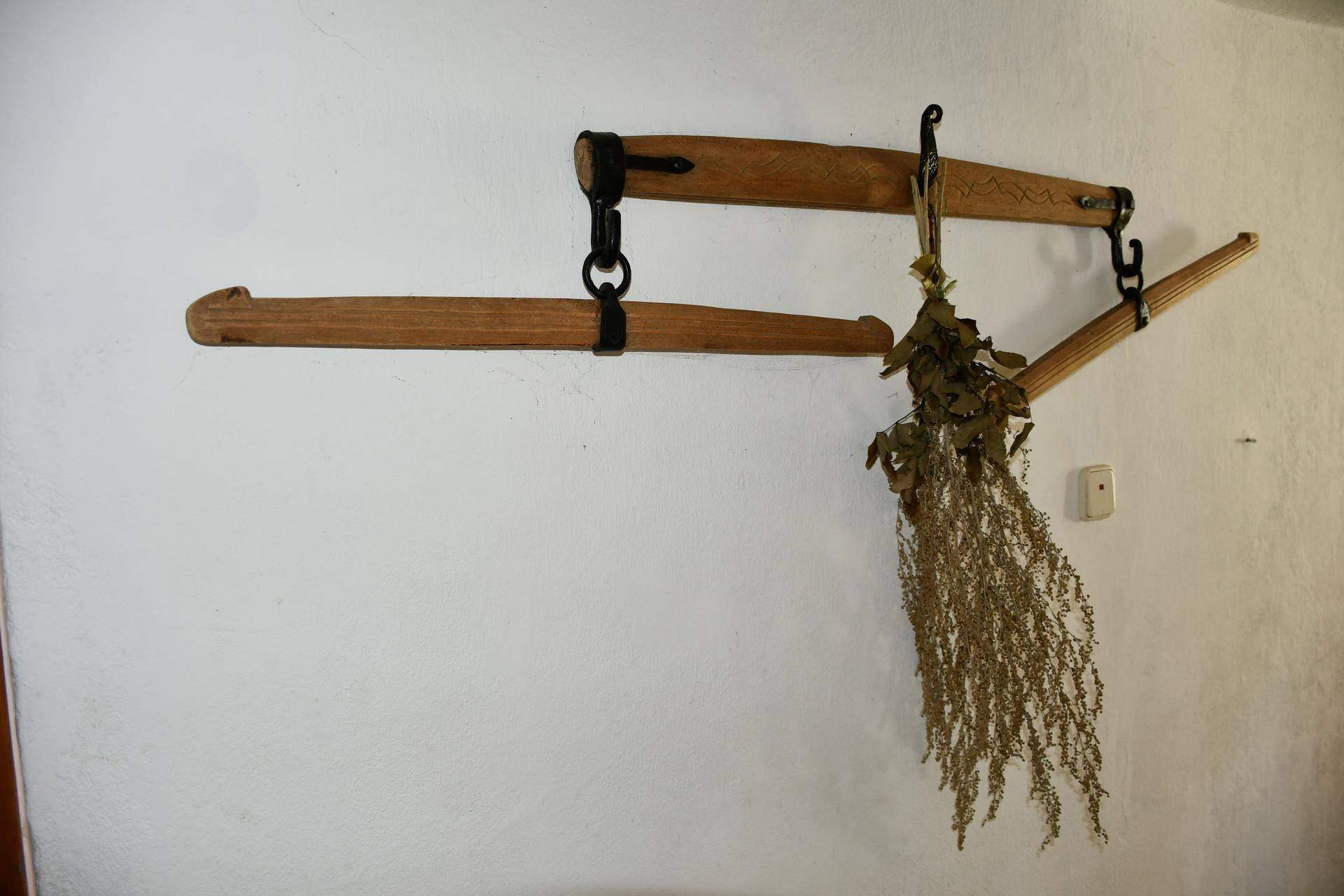 Rustikale Wanddekoration aus Holz mit getrockneten Kräutern, die an einer weißen Wand hängt.