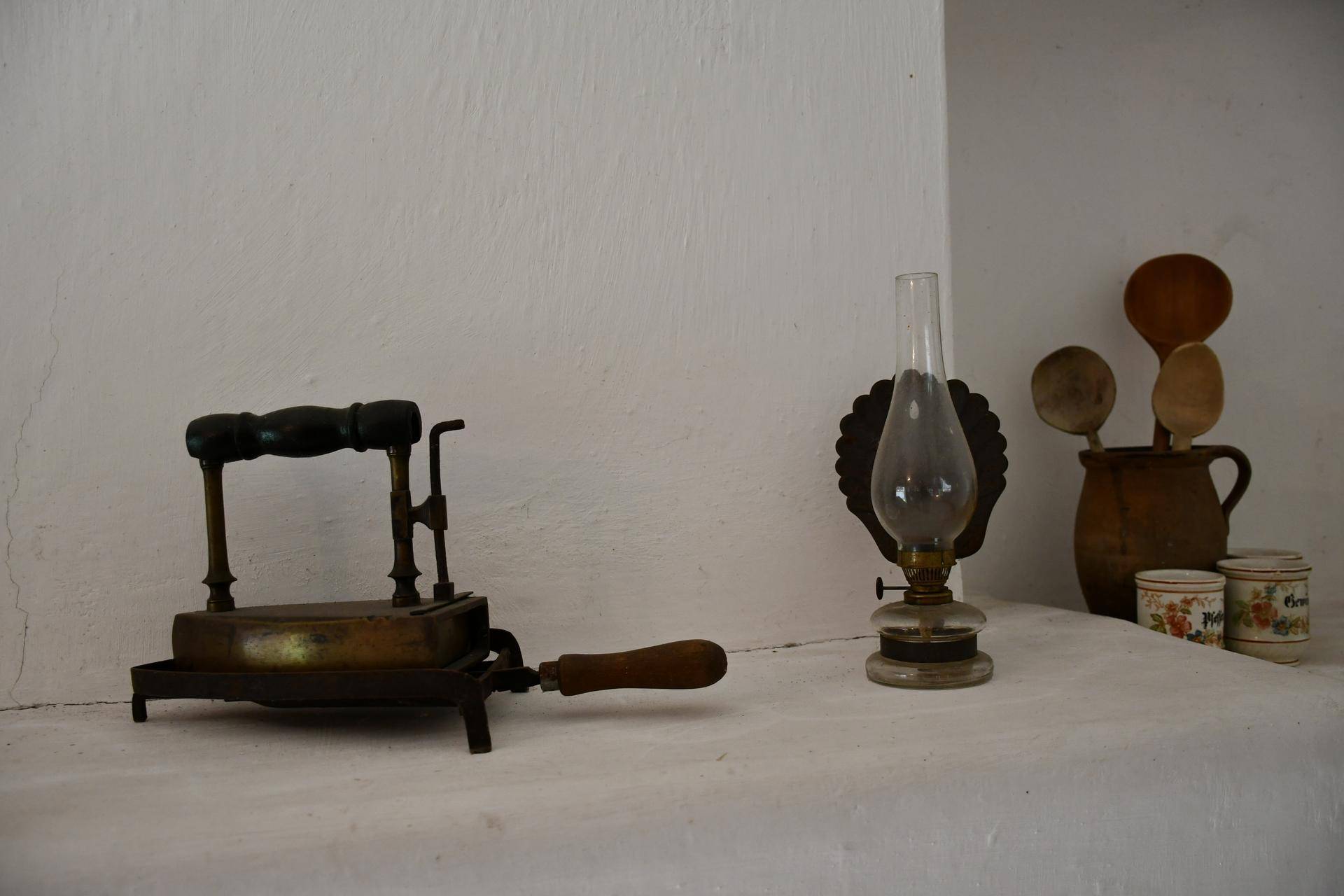 Historische Haushaltsgegenstände wie ein altes Bügeleisen und eine Petroleumlampe auf einer Ablage.