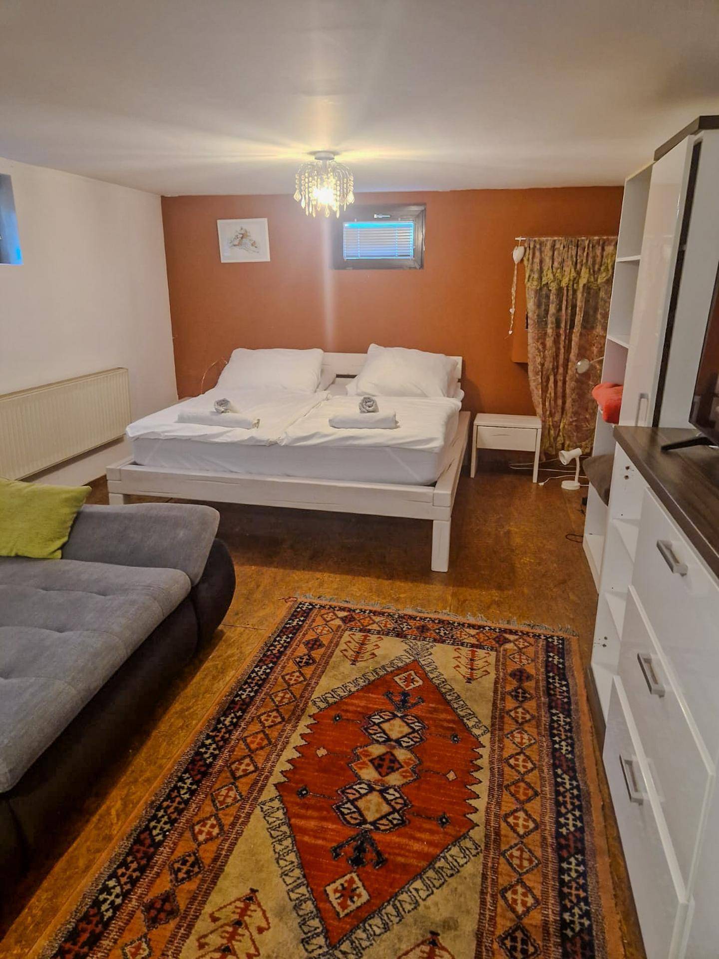 Kombiniertes Schlaf- und Wohnzimmer mit Bett, Sofa und TV-Möbeln, akzentuiert durch eine orangefarbene Wand.