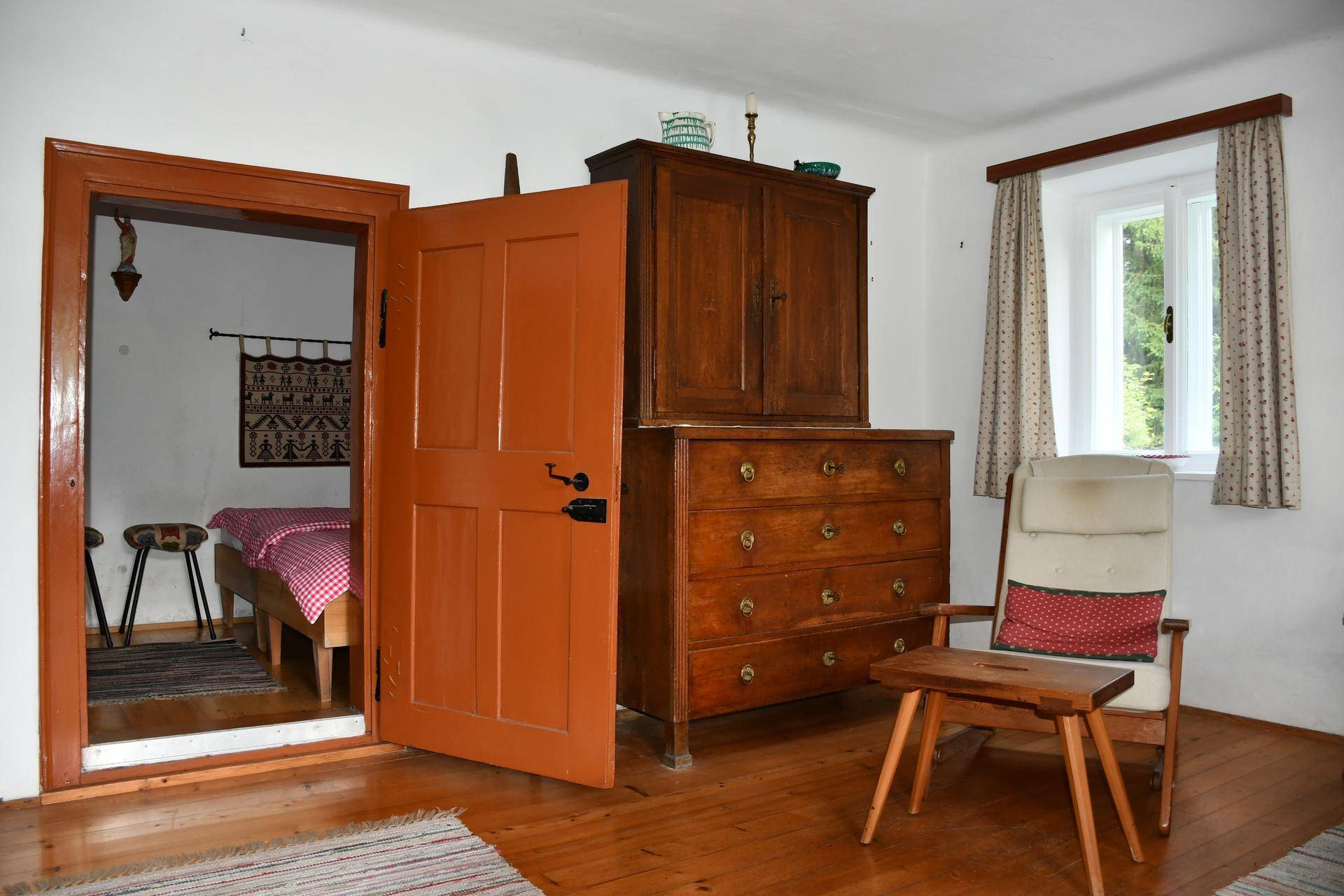 Gemütlicher Wohnbereich mit Sessel, antiken Möbeln und Zugang zu einem Schlafzimmer.