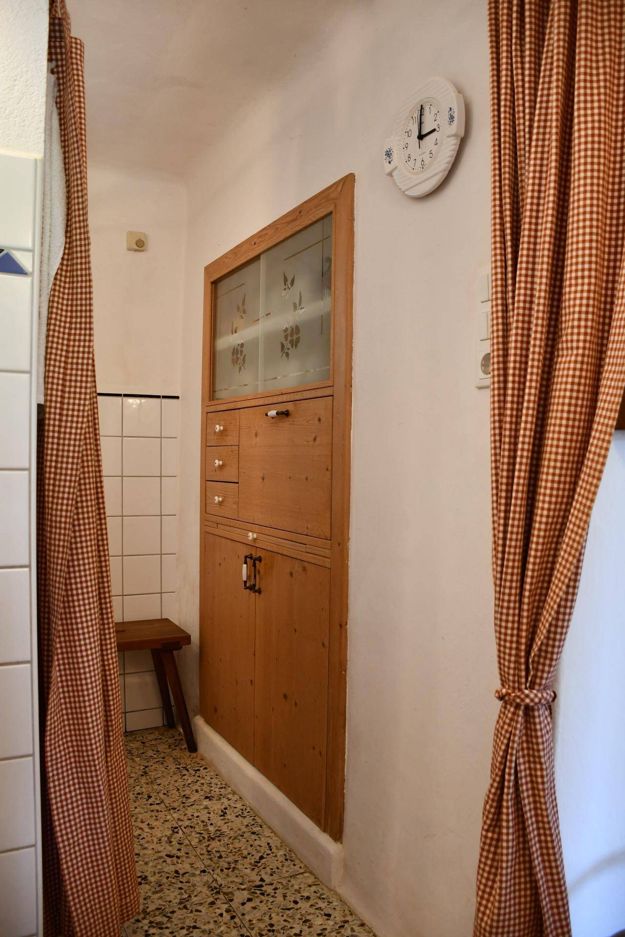 Eingebauter traditioneller Holzschrank mit Glastüren und Schubladen, umgeben von karierten Vorhängen.