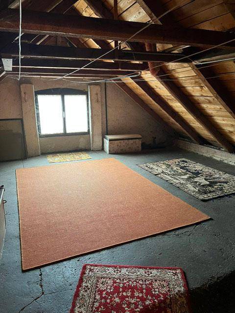 Geräumiges Dachgeschoss mit sichtbaren Holzbalken, schrägen Wänden und Fenstern.
