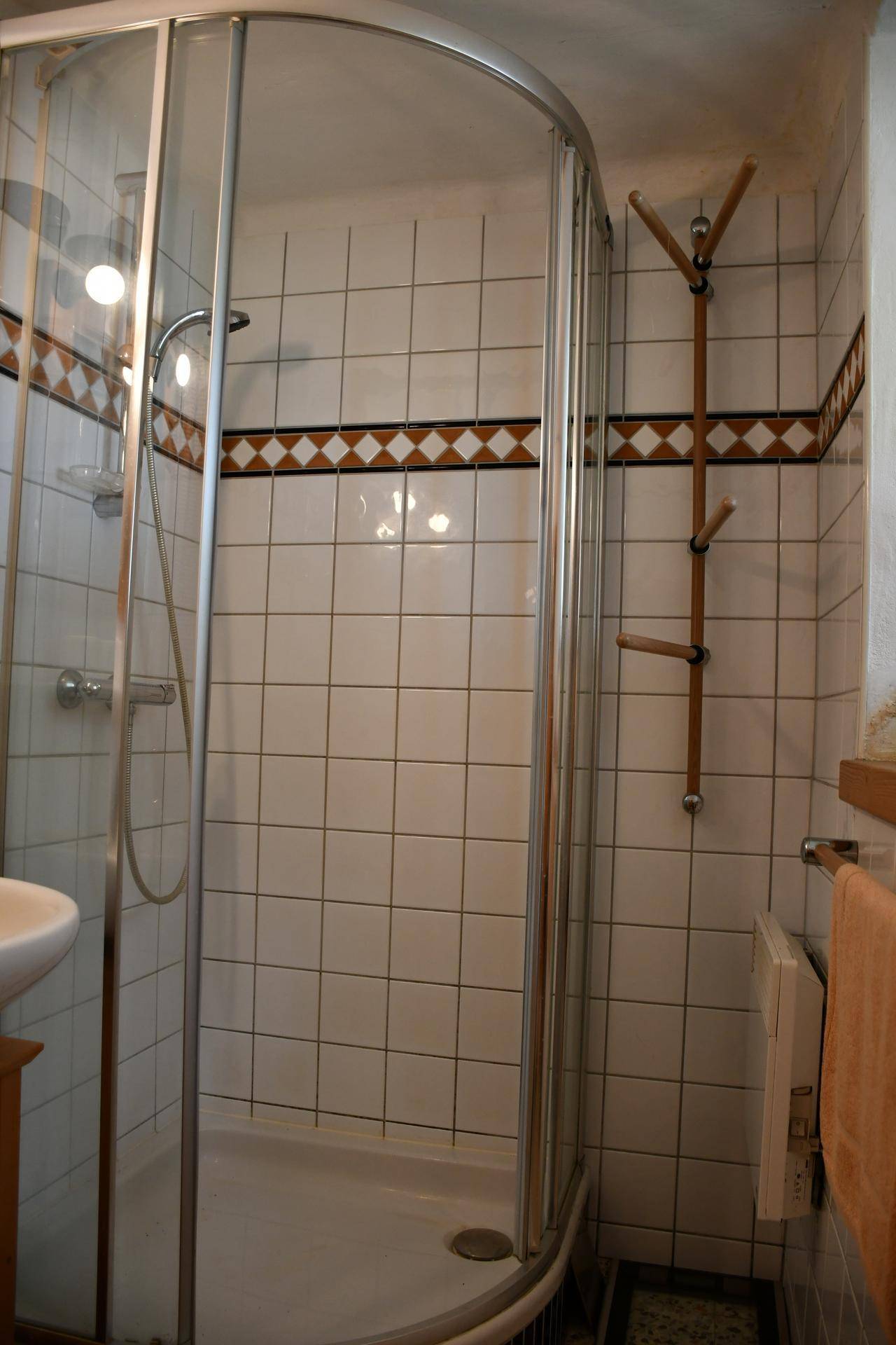 Duschkabine in einem einfach gefliesten Badezimmer mit weiß-braunen Akzenten und Handtuchhalter.