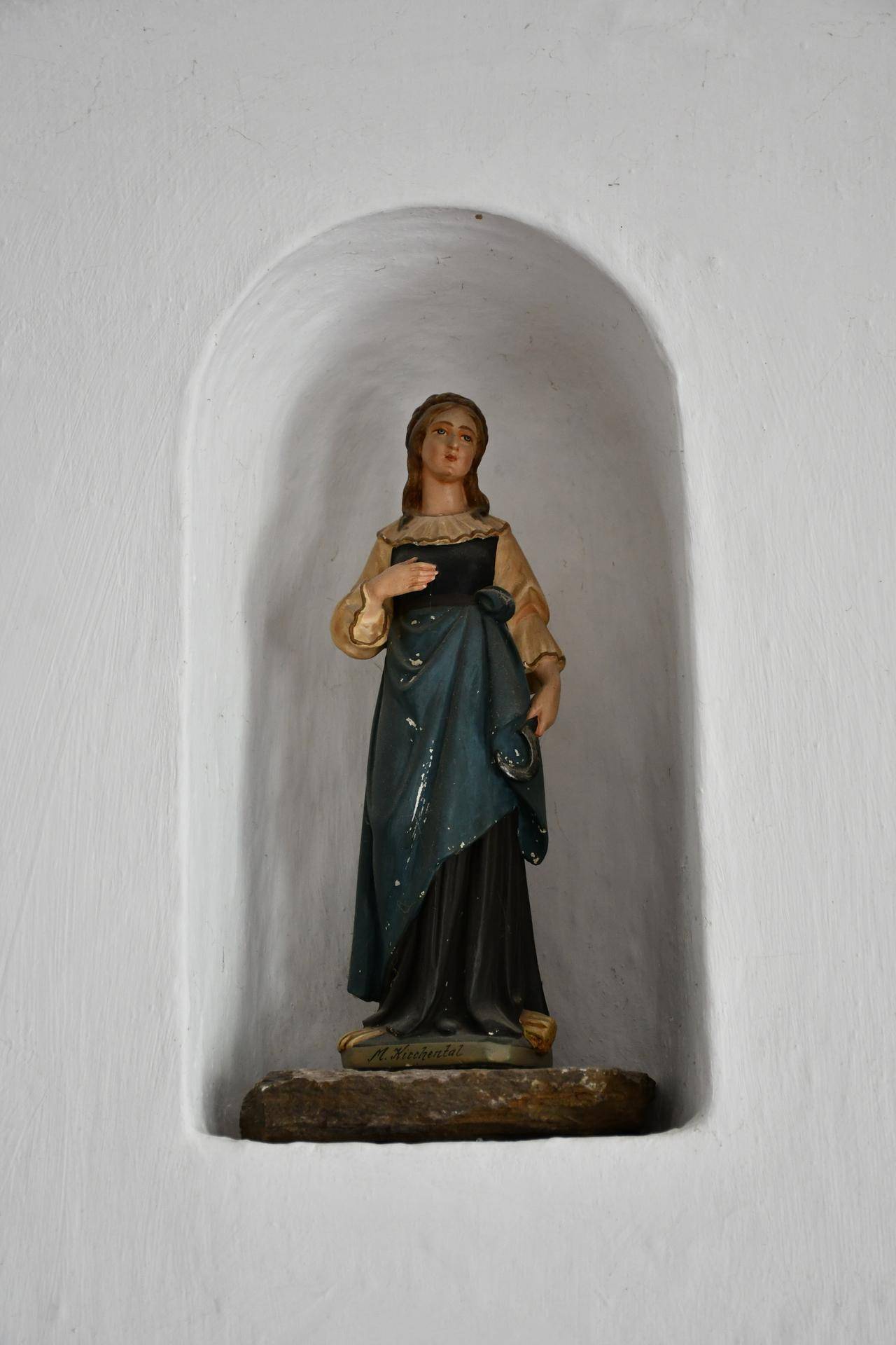 Eine religiöse Statue in einer weißen Wandnische, die eine weibliche Figur darstellt.