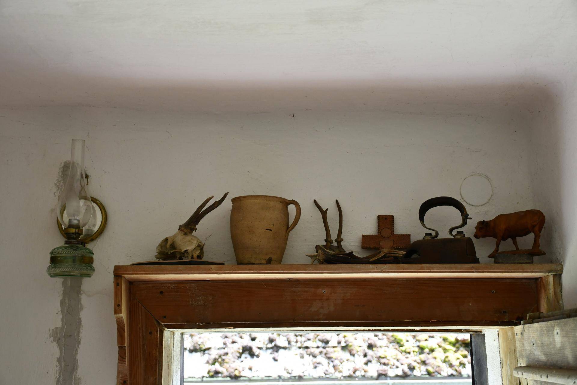 Eine Petroleumlampe und traditionelle Dekorationsgegenstände wie Geweihe auf einem Holzregal über einer Tür.
