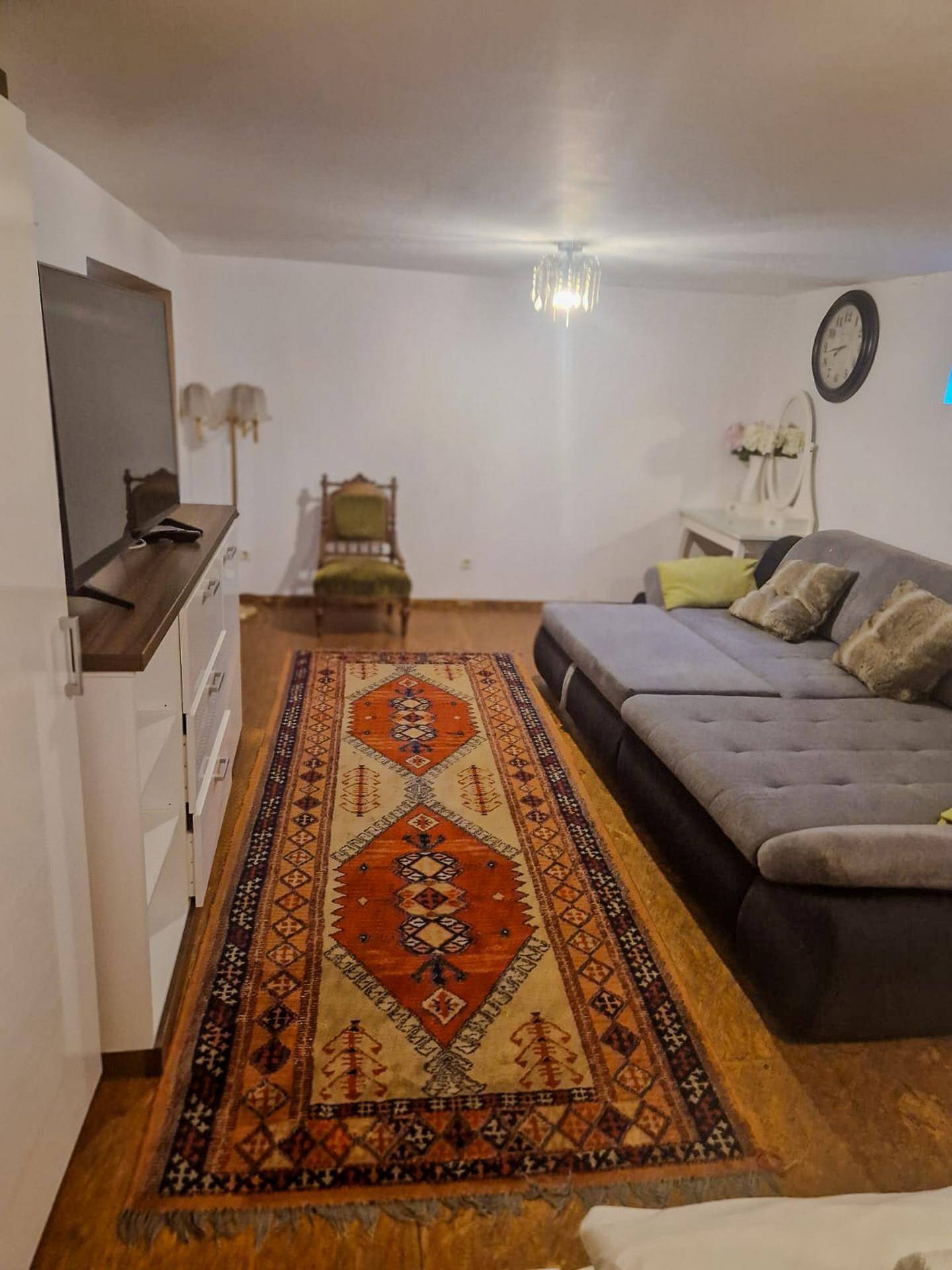 Geräumiges Wohnzimmer mit großem Ecksofa, Fernseher und einem traditionellen Teppich auf Holzboden.