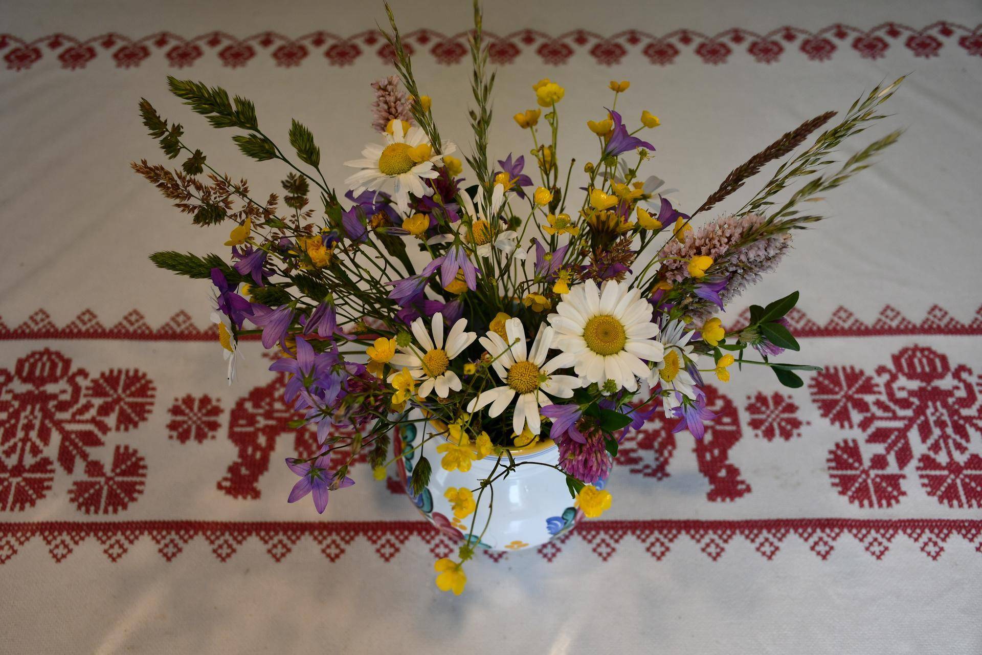 Bunter Wildblumenstrauß in einer Vase auf einem traditionell bestickten Tischtuch, das Gemütlichkeit ausstrahlt.