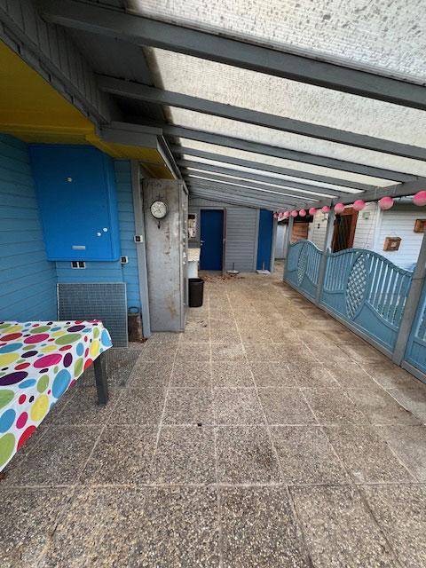 Langer überdachter Terrassenbereich mit gepflastertem Boden und blauer Holzverkleidung.