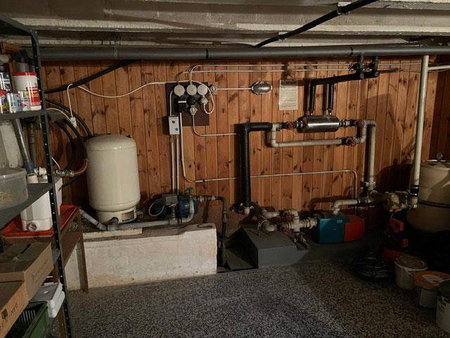Heizungsraum im Keller mit Rohren und technischen Installationen an der Holzwand.