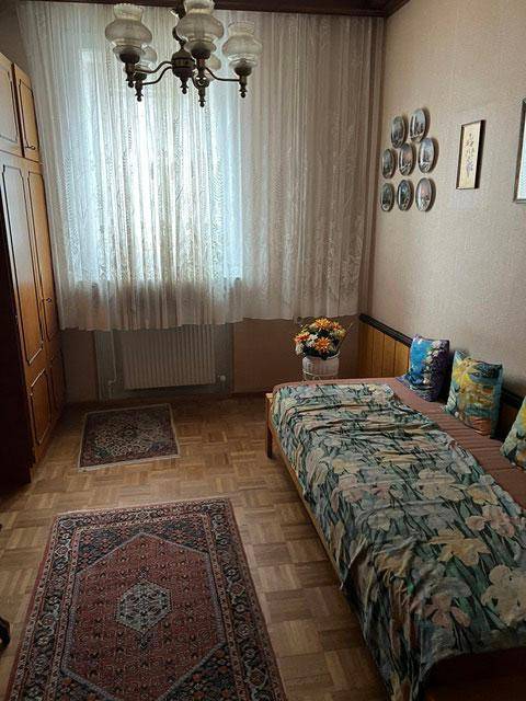 Schlafzimmer mit Einzelbett, Holzparkett, Teppich und Fenster mit Vorhängen.