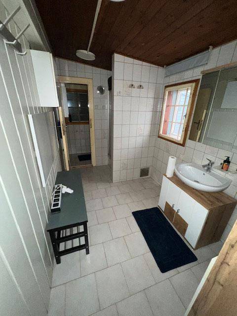 Badezimmer mit Fliesenboden, Holzdecke und einem Waschbecken mit Unterschrank.