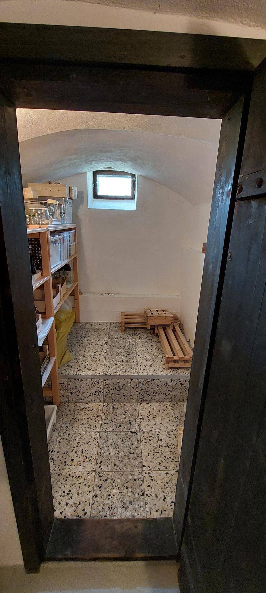 Gewölbekeller mit Regalen für Lagerung, gefliestem Boden und einem kleinen Fenster für Belüftung.