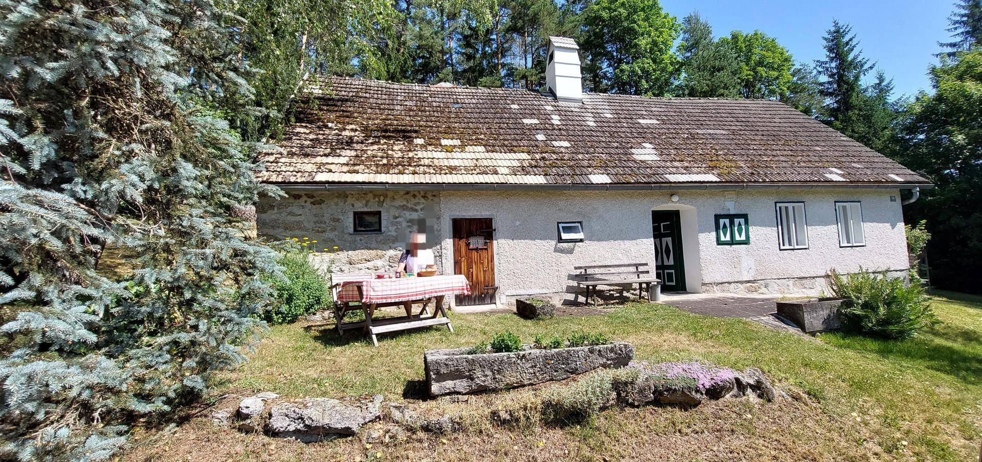 Rustikales Landhaus mit Sitzgelegenheit im Garten, umgeben von Bäumen und ländlicher Idylle.