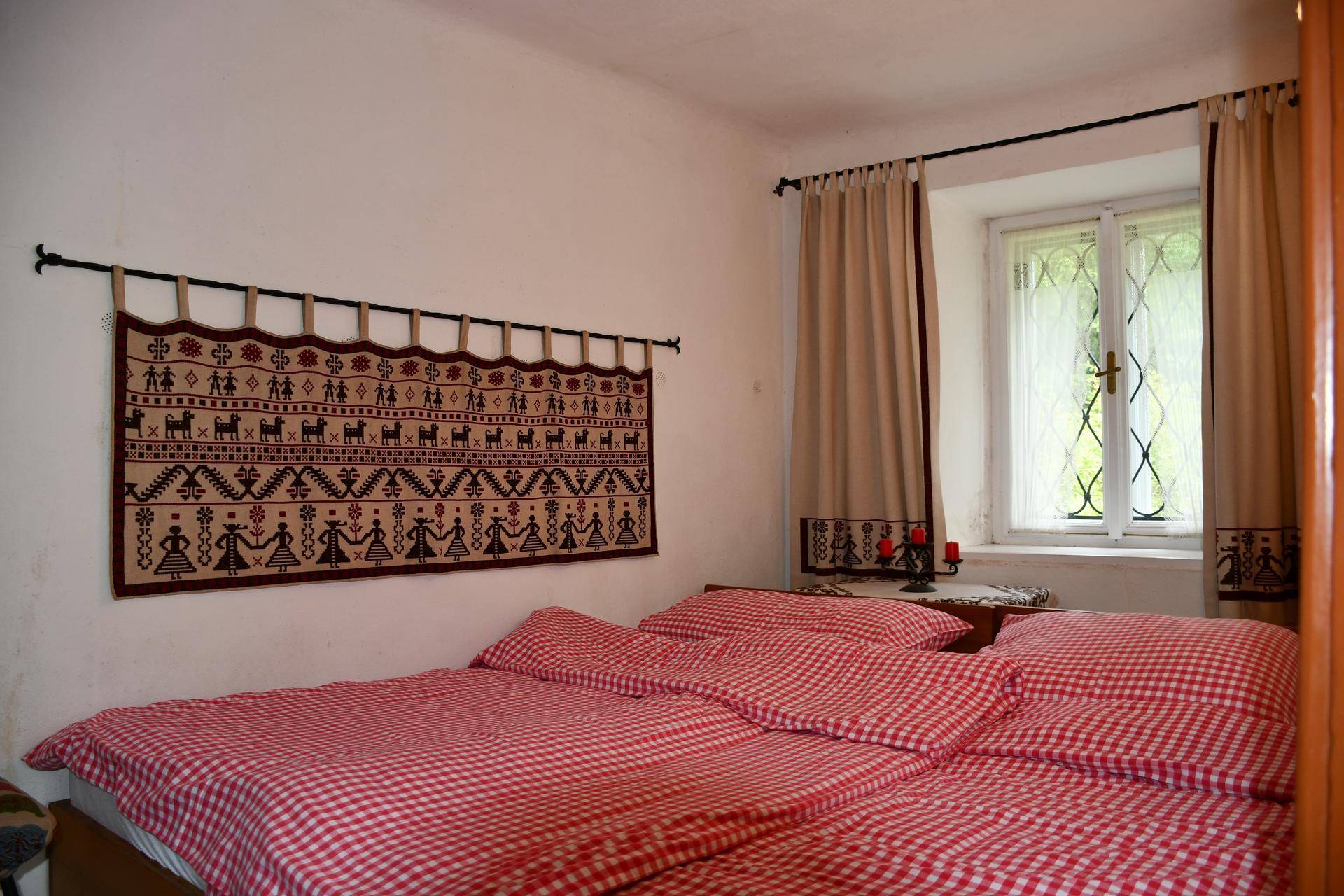 Schlafzimmer mit traditioneller Wanddekoration, karierter Bettwäsche und einem Fenster mit Vorhängen.