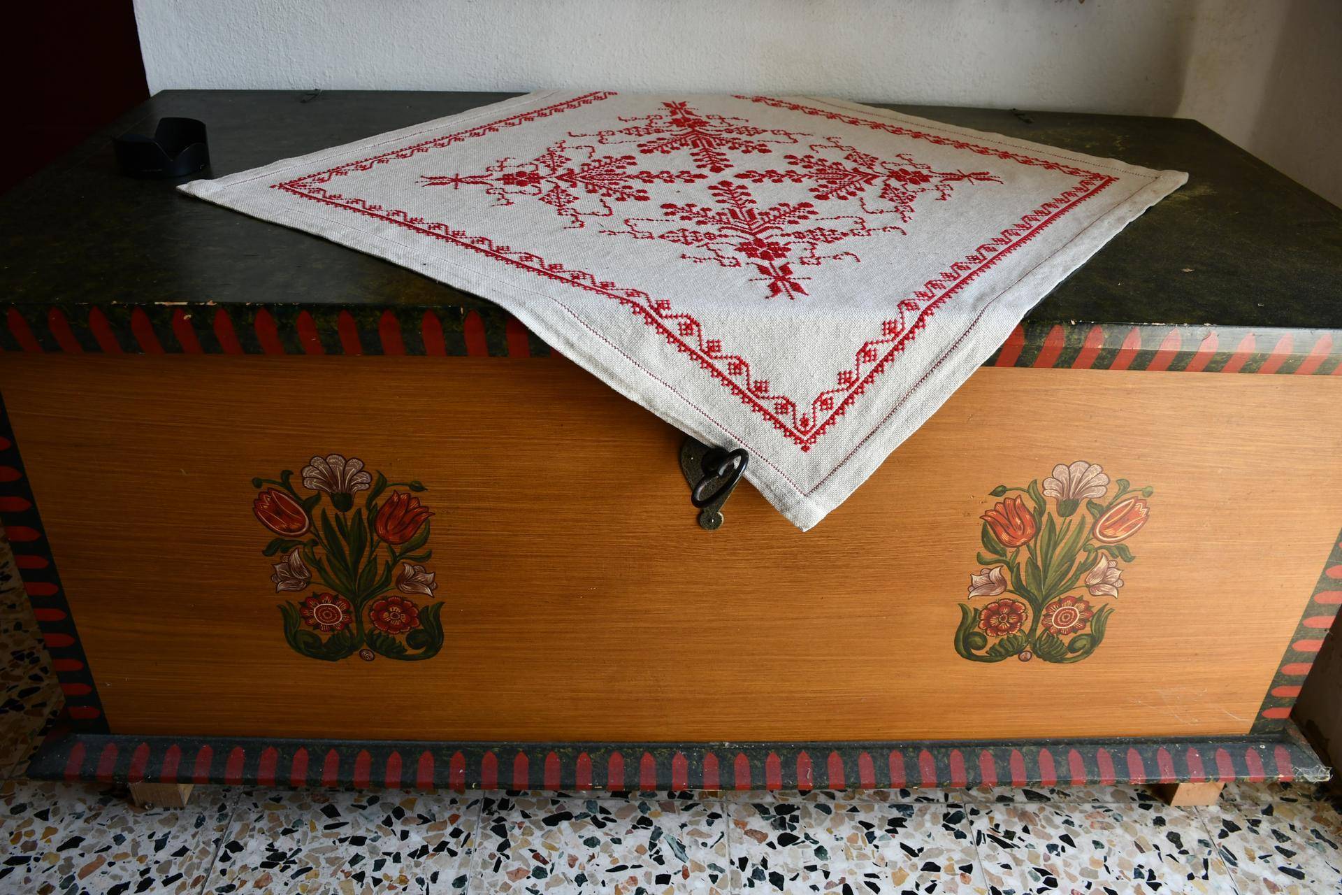 Eine alte, bemalte Holztruhe mit traditionellem Muster und bestickter Tischdecke.