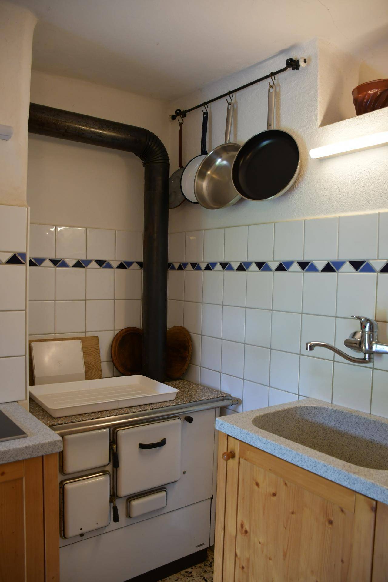 Traditionelle Küche mit Holzofen, weißen Fliesen und blauen Akzenten, sowie rustikalen Holzschränken und Spüle.