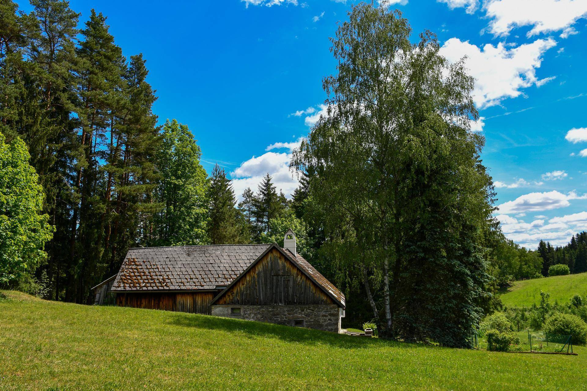 Malerisches Landhaus in ländlicher Umgebung, umgeben von Wiesen und hohen Bäumen.