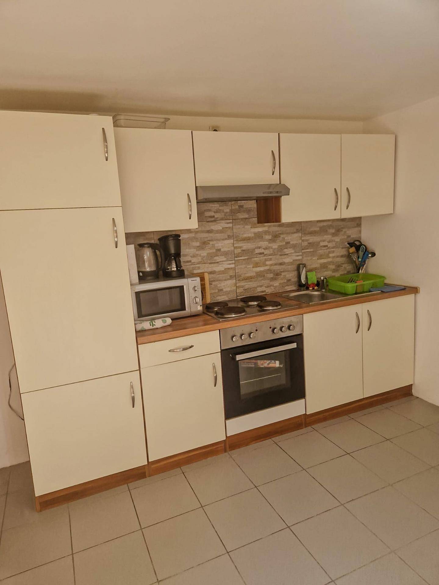 Kompakte Küche mit weißen Schränken, integriertem Backofen und Mikrowelle, ideal für kleine Haushalte.