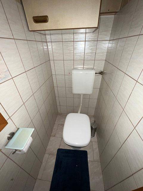 Kleines separates WC mit hellen Fliesen und einem wandmontierten Spülkasten.