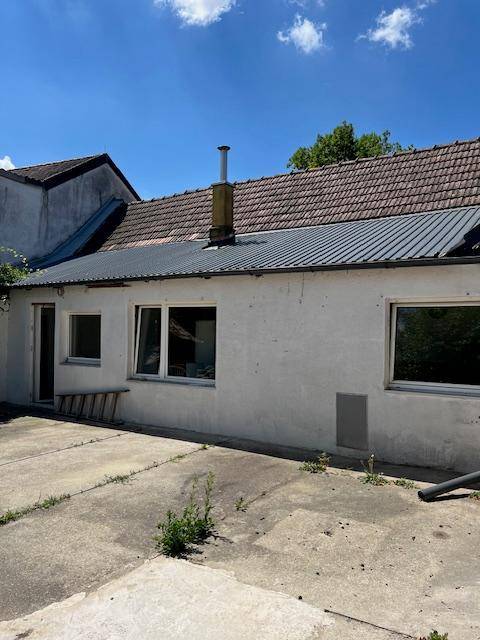 Rückseite eines Hauses mit weißer Fassade, Fenstern und einer gepflasterten Fläche.