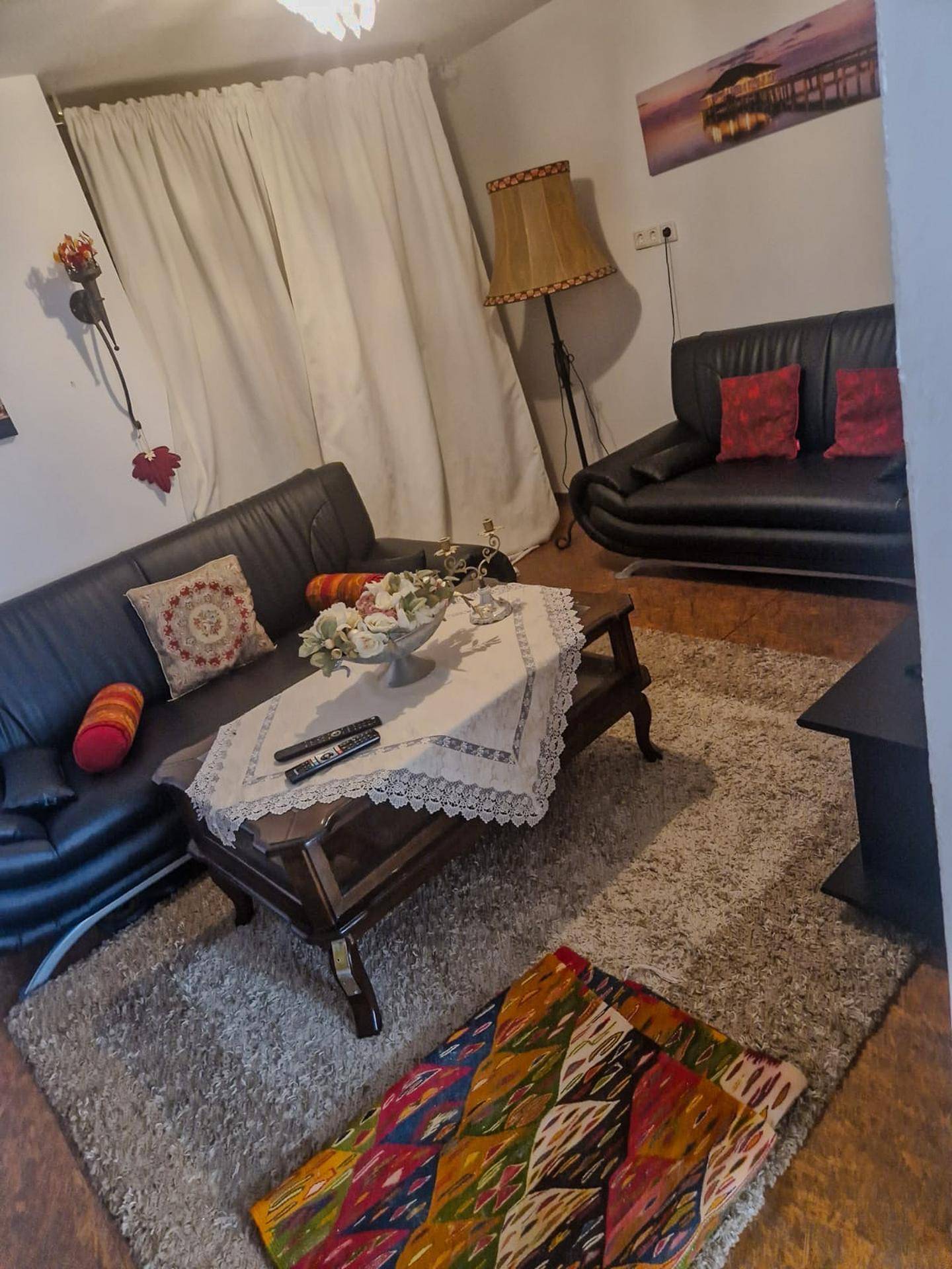 Gemütliches Wohnzimmer mit zwei schwarzen Sofas, Couchtisch und Fernseher, auf einem flauschigen Teppich.