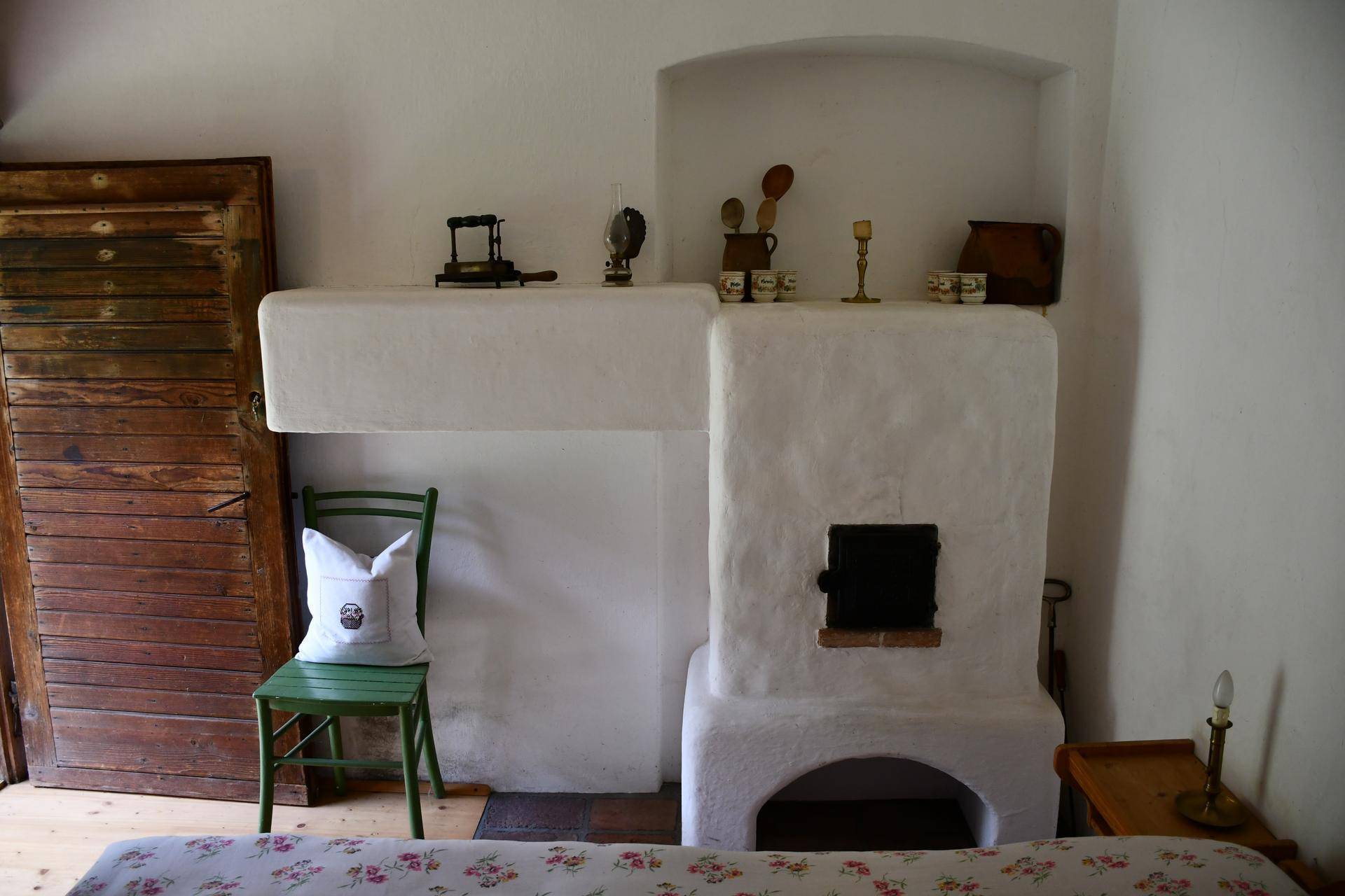 Traditioneller weißer Kamin mit Ablagefläche und einem grünen Stuhl in einem rustikalen Wohnbereich.