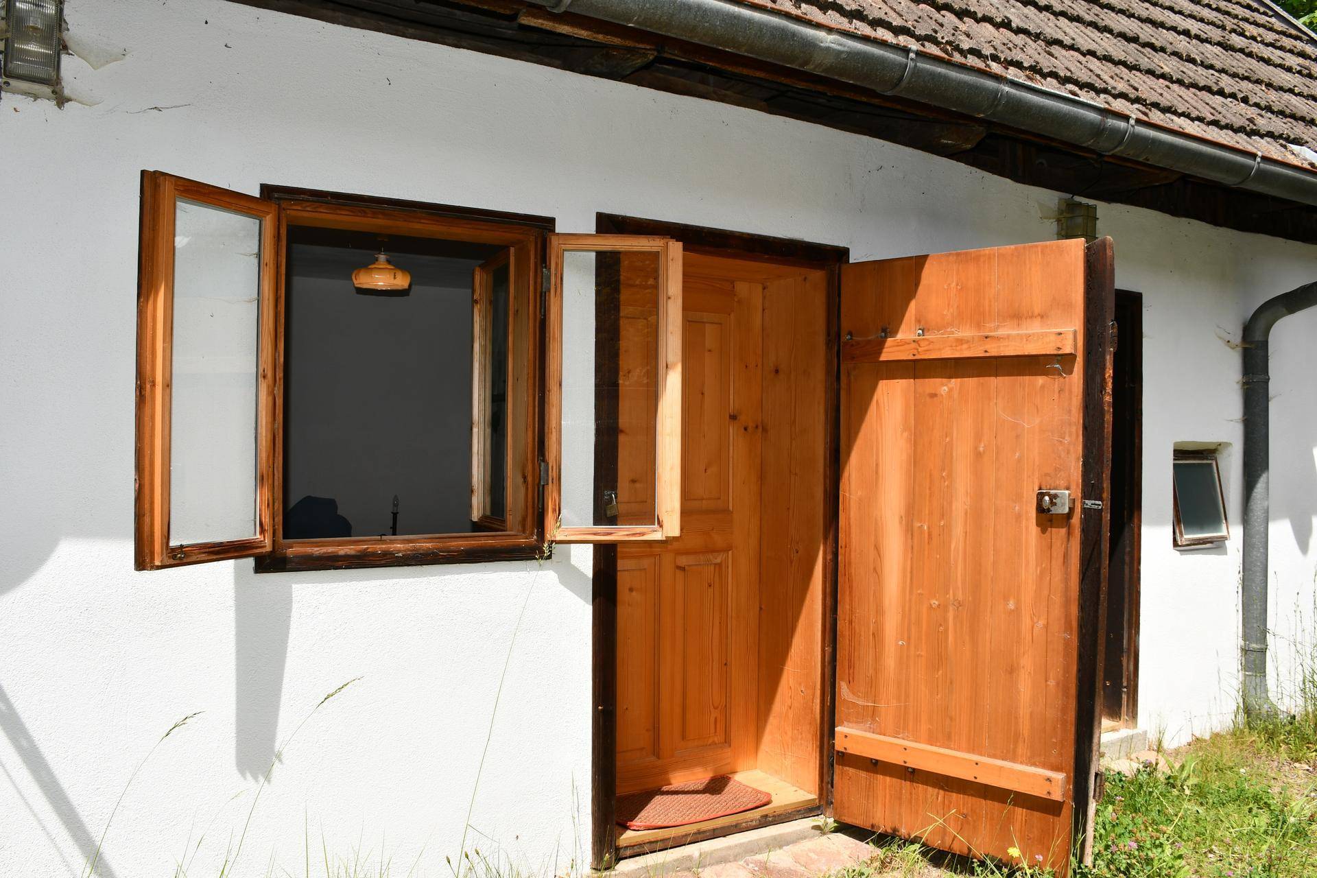 Weiße Hausfassade mit offener Holztür und Fenster, die einen Einblick in den Innenraum gewähren.